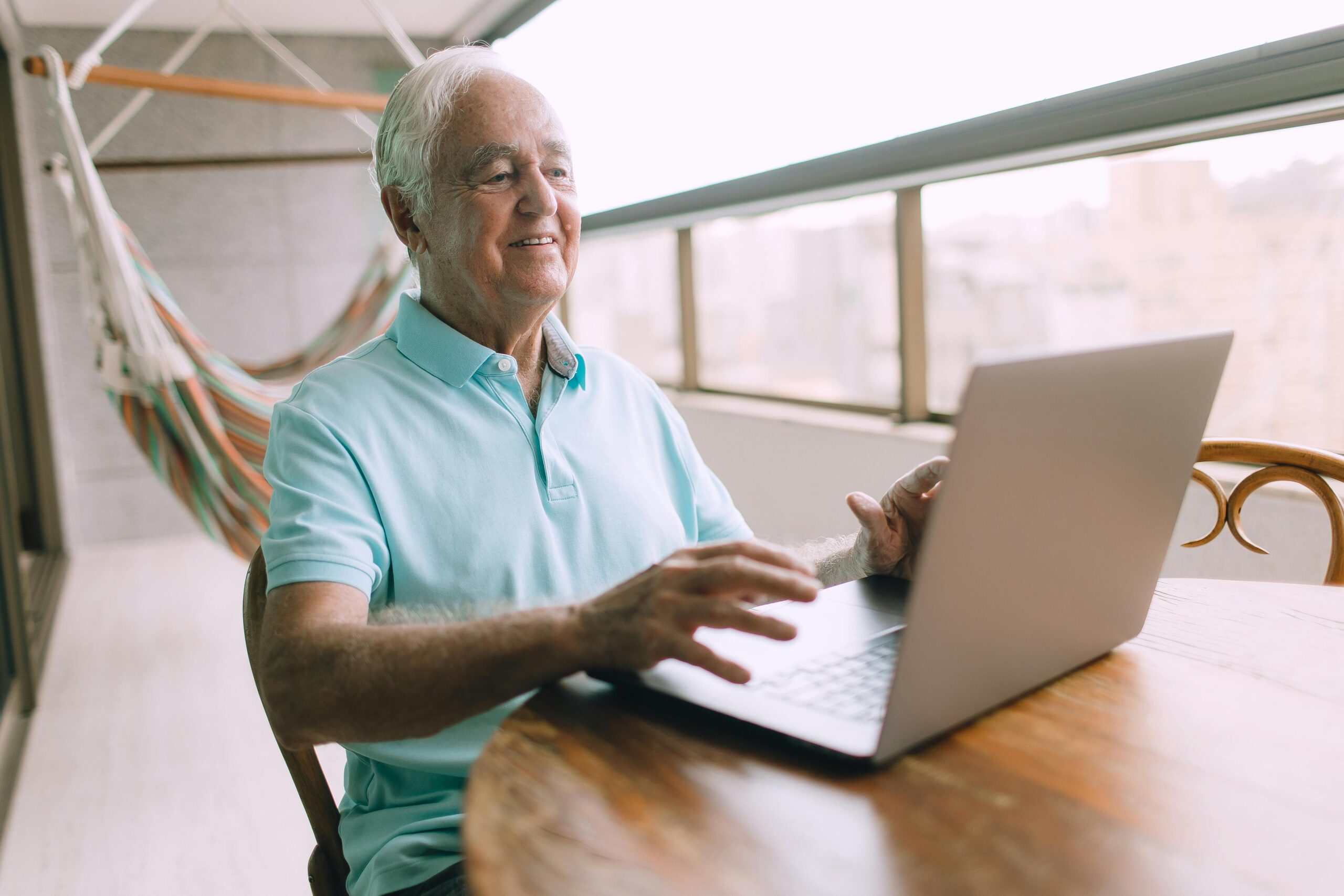 elderly man using laptop at a table next to the window